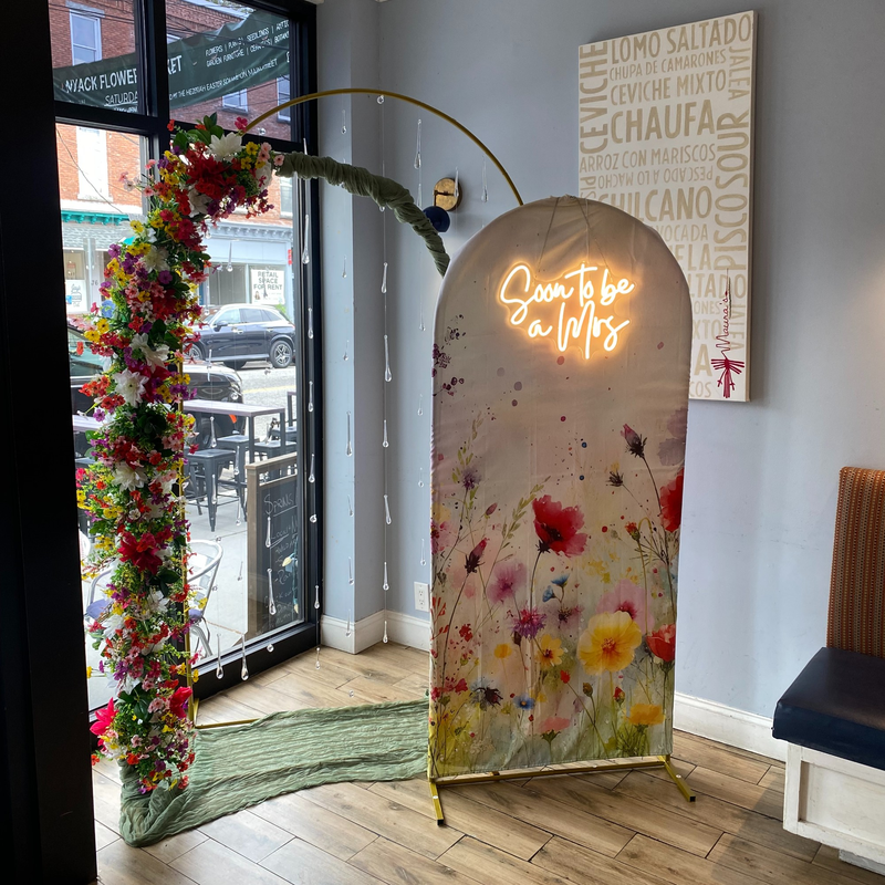 A floral arch and a neon sign set up for a bridal shower